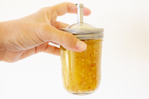 A hand holding a jar full of salad dressing.