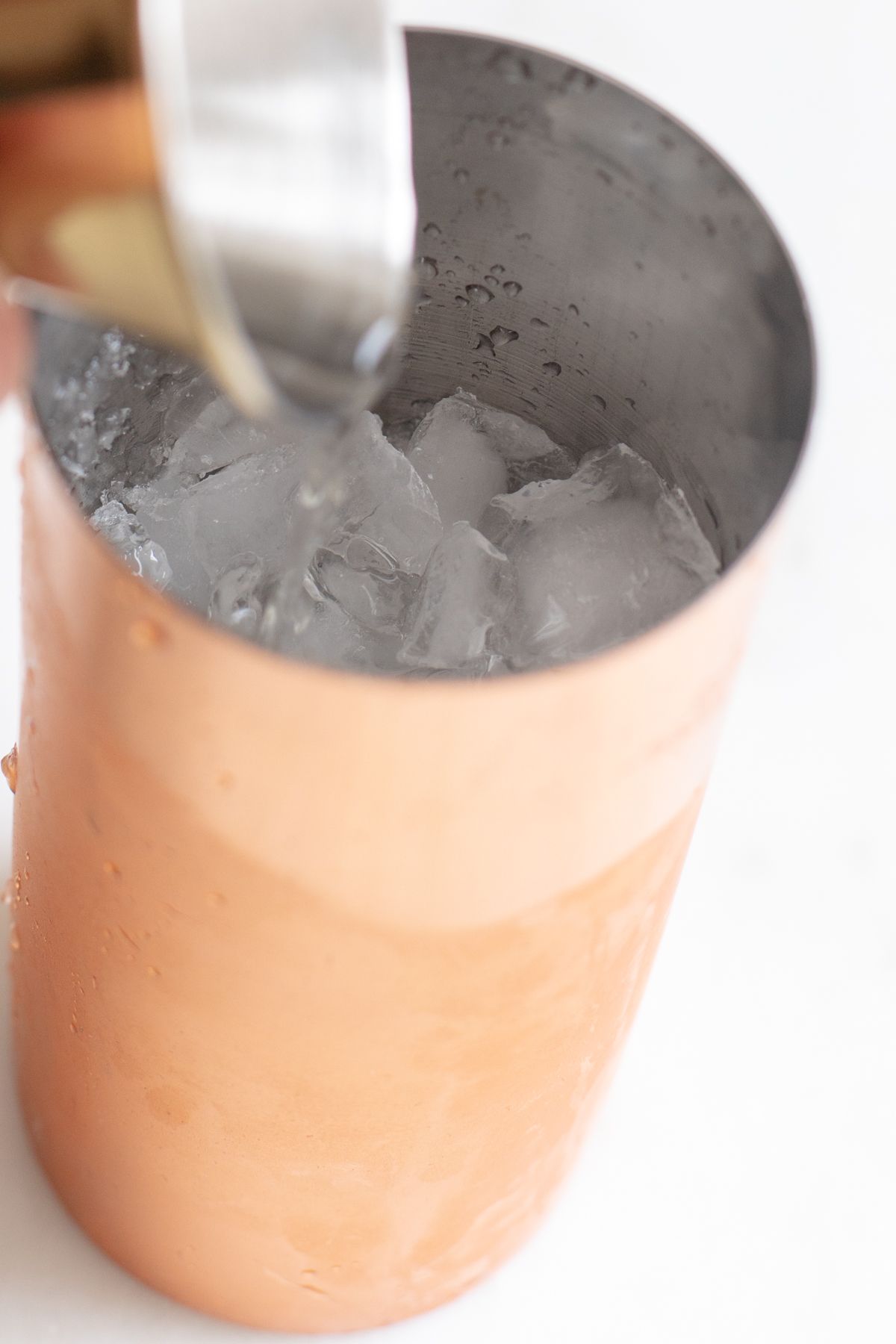 A copper shaker with a hand mixing up Cadillac margarita ingredients.