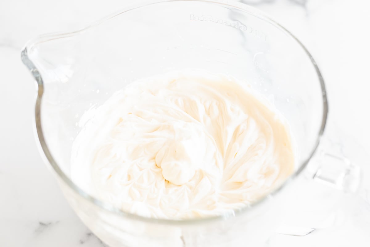 Condensed milk ice cream being whipped in the glass bowl of a stand mixer.