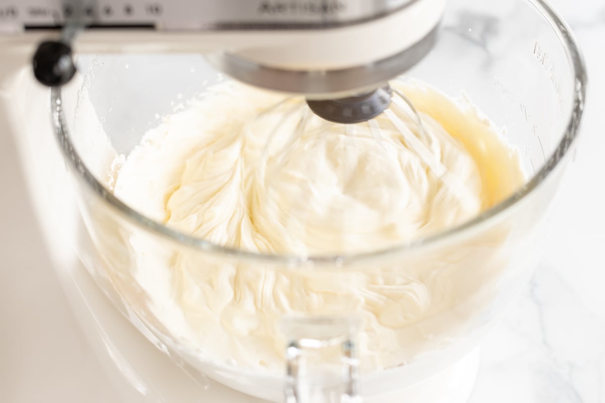 Condensed milk ice cream being whipped in the glass bowl of a stand mixer.