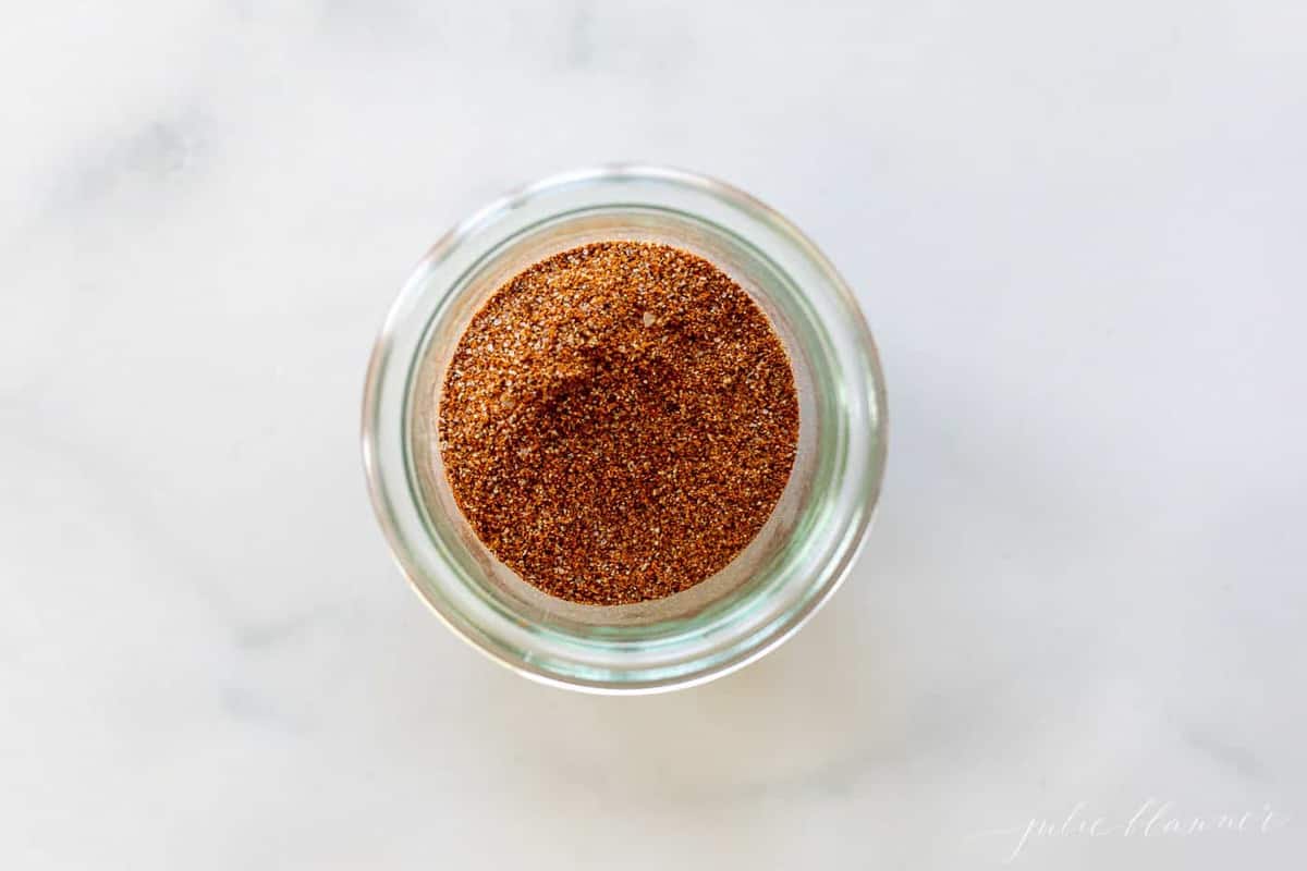 A marble surface with a clear glass jar full of homemade fajita seasoning mix.