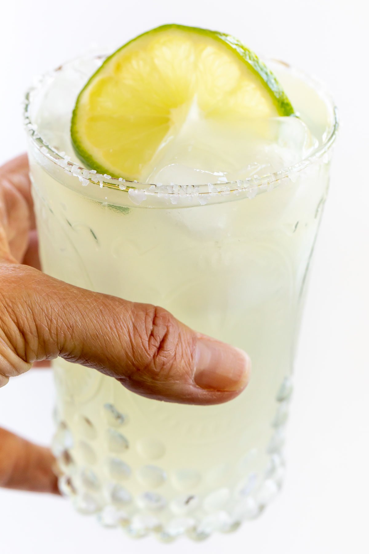 A hand holding a glass of a homemade margarita recipe