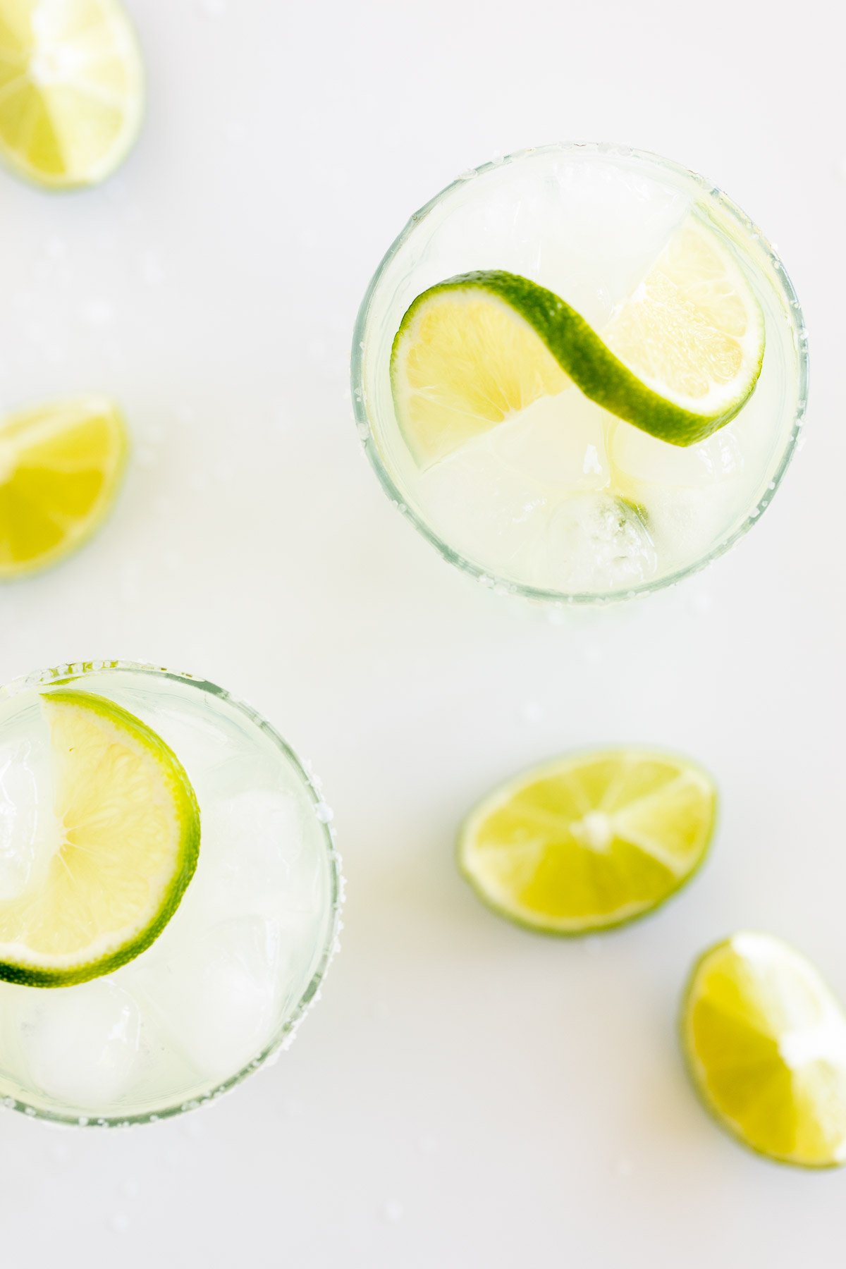 margarita glasses on a white countertop, with slices of limes. 