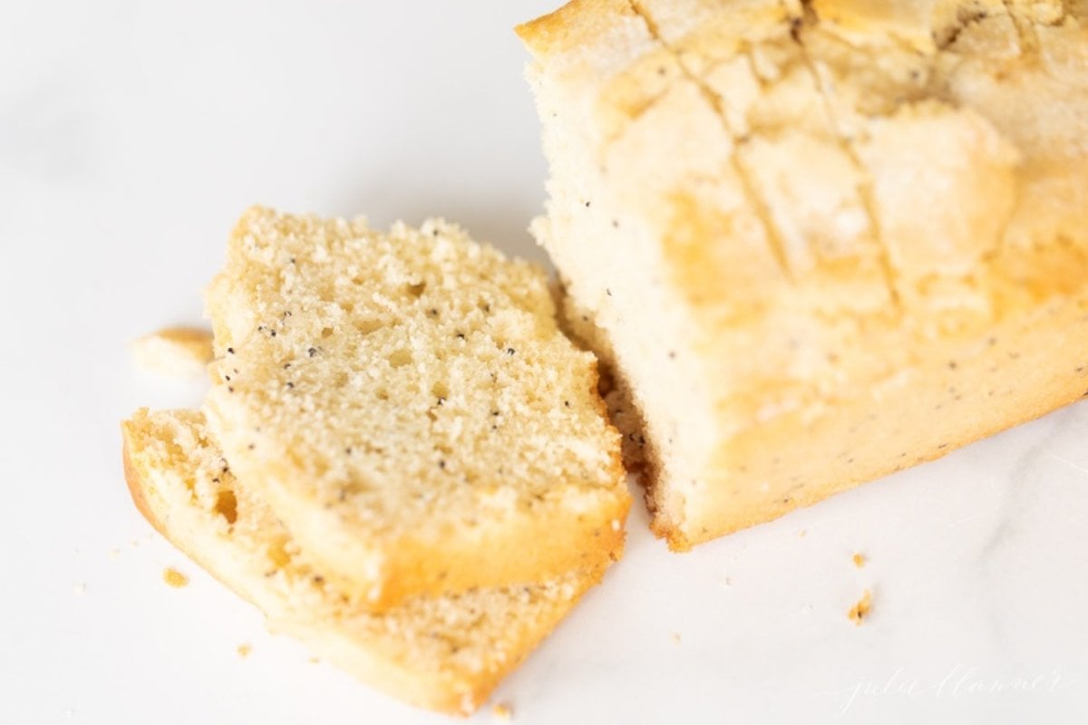 A poppy seed loaf of bread, sliced on a marble countertop.