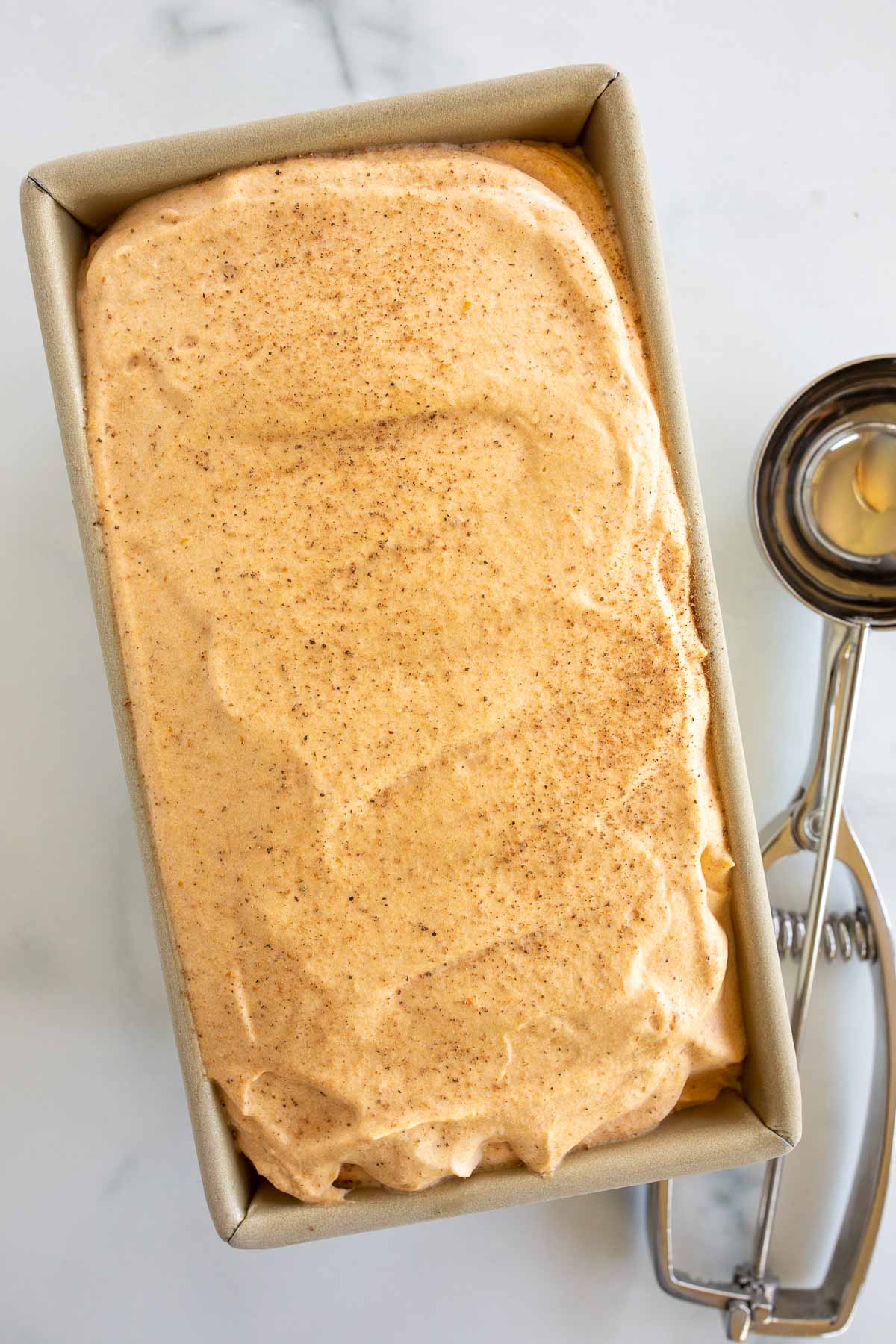 A gold metal loaf pan filled with a no churn ice cream recipe, with a scoop on top.