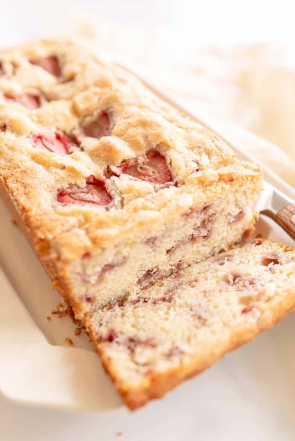 A close-up of a sliced loaf of strawberry bread, showcasing the moist interior with visible pieces of strawberries. The delectable strawberry bread is placed on a white surface, inviting you to try this delightful strawberry bread recipe.