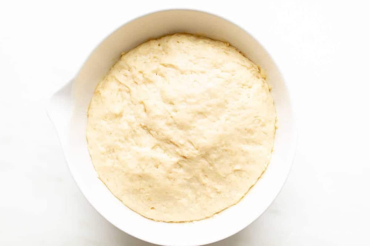 A white bowl filled with dough made with yeast.