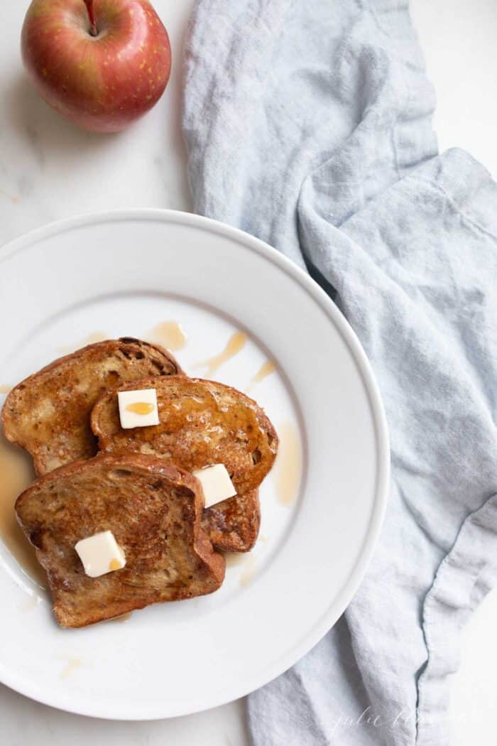 Apple fritter french toast topped with butter and syrup on a white plate.