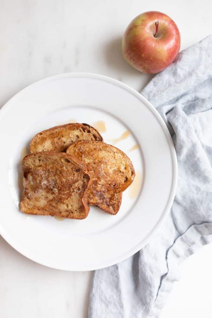 Apple fritter french toast topped with syrup on a white plate.