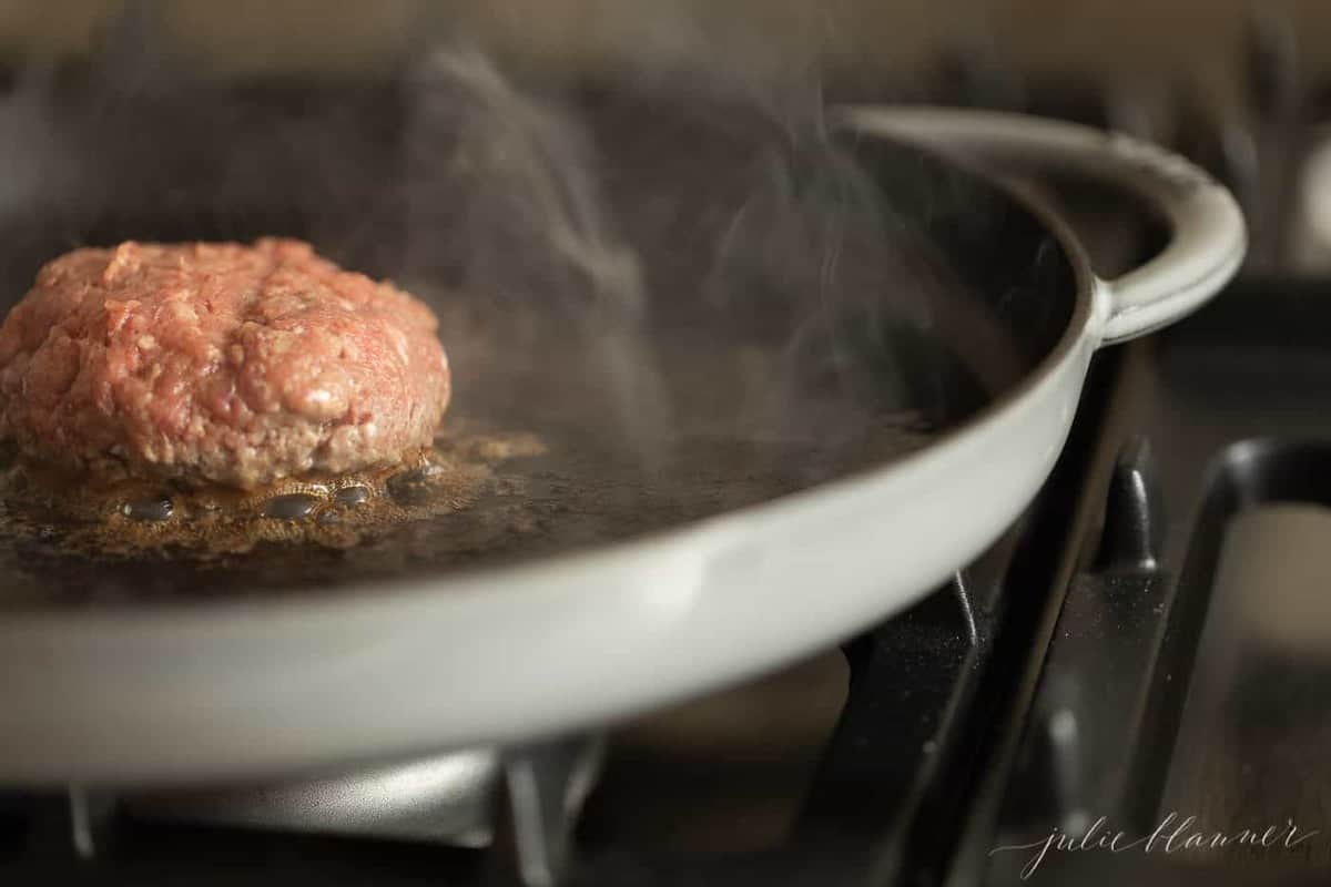 A burger being cooked in a cast iron pan. 