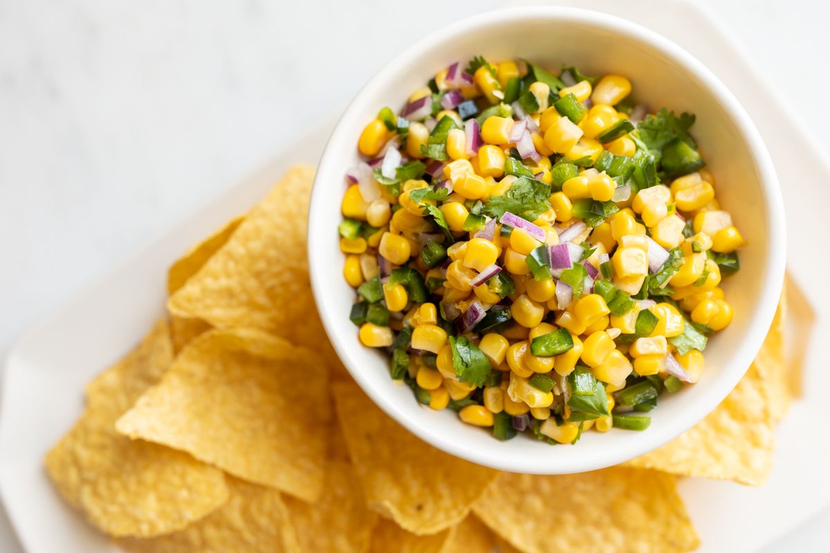 A chipotle corn salsa recipe in a white bowl, placed on a white platter full of corn tortilla chips 