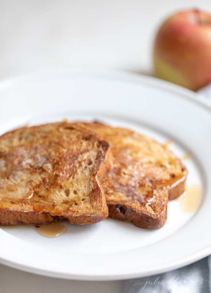 Apple fritter french toast topped with syrup on a white plate.