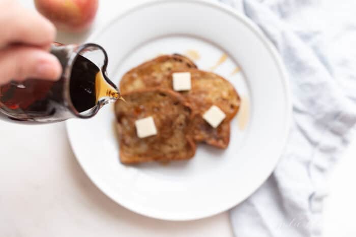 Apple fritter french toast topped with butter and syrup on a white plate.