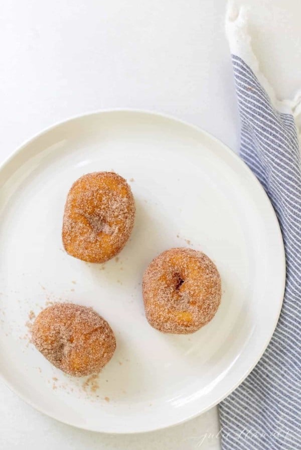 A white plate with three biscuit donuts covered in cinnamon sugar.