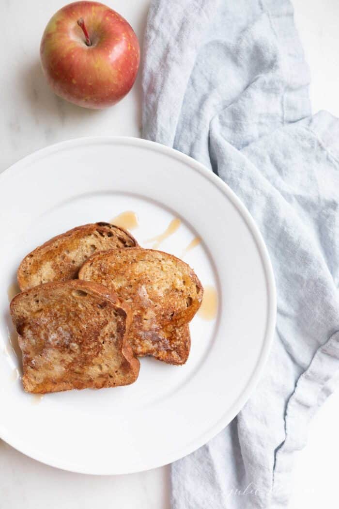 Apple fritter french toast topped with syrup on a white plate.