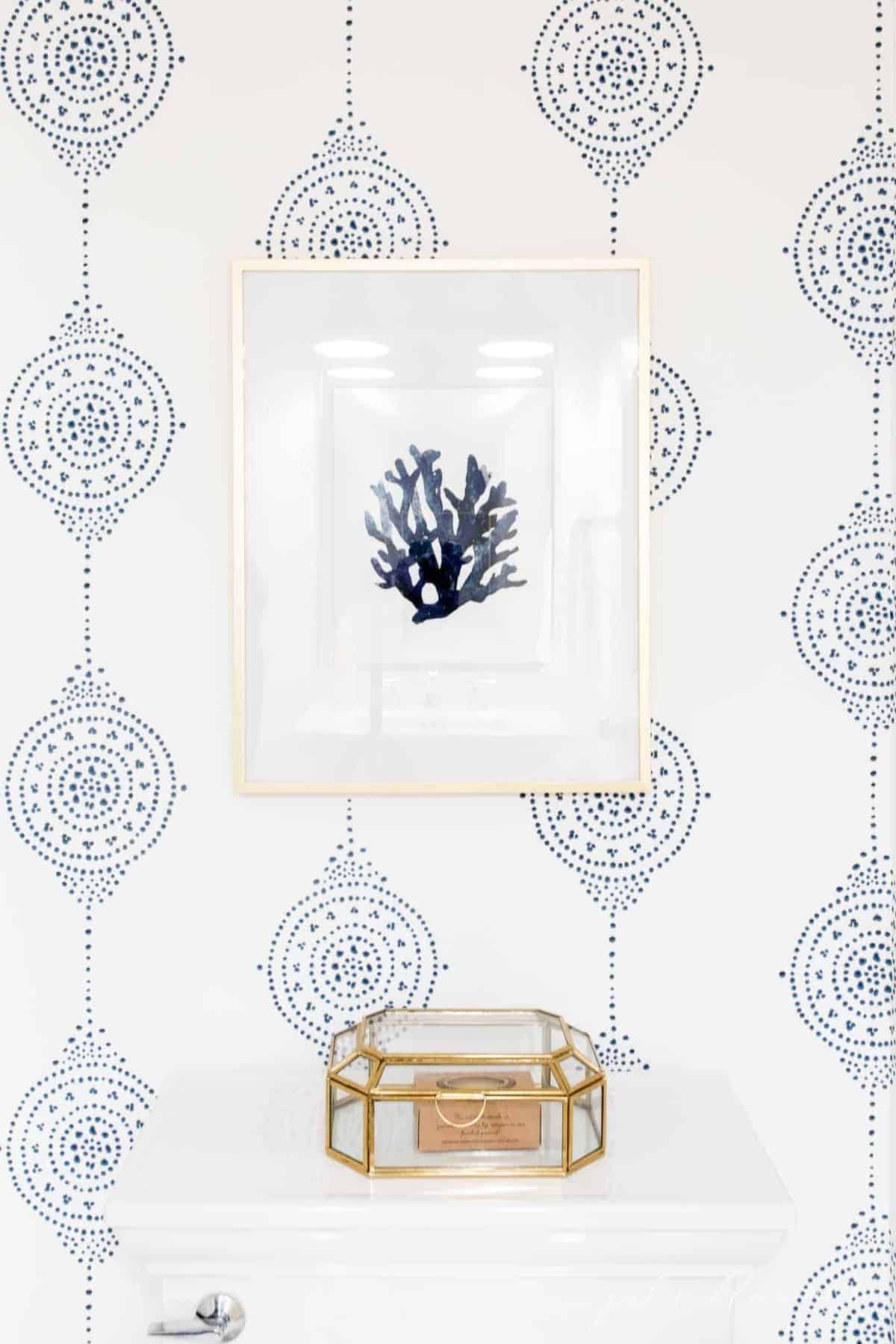 Blue and white patterned bathroom wallpaper with seashell art over the toilet.