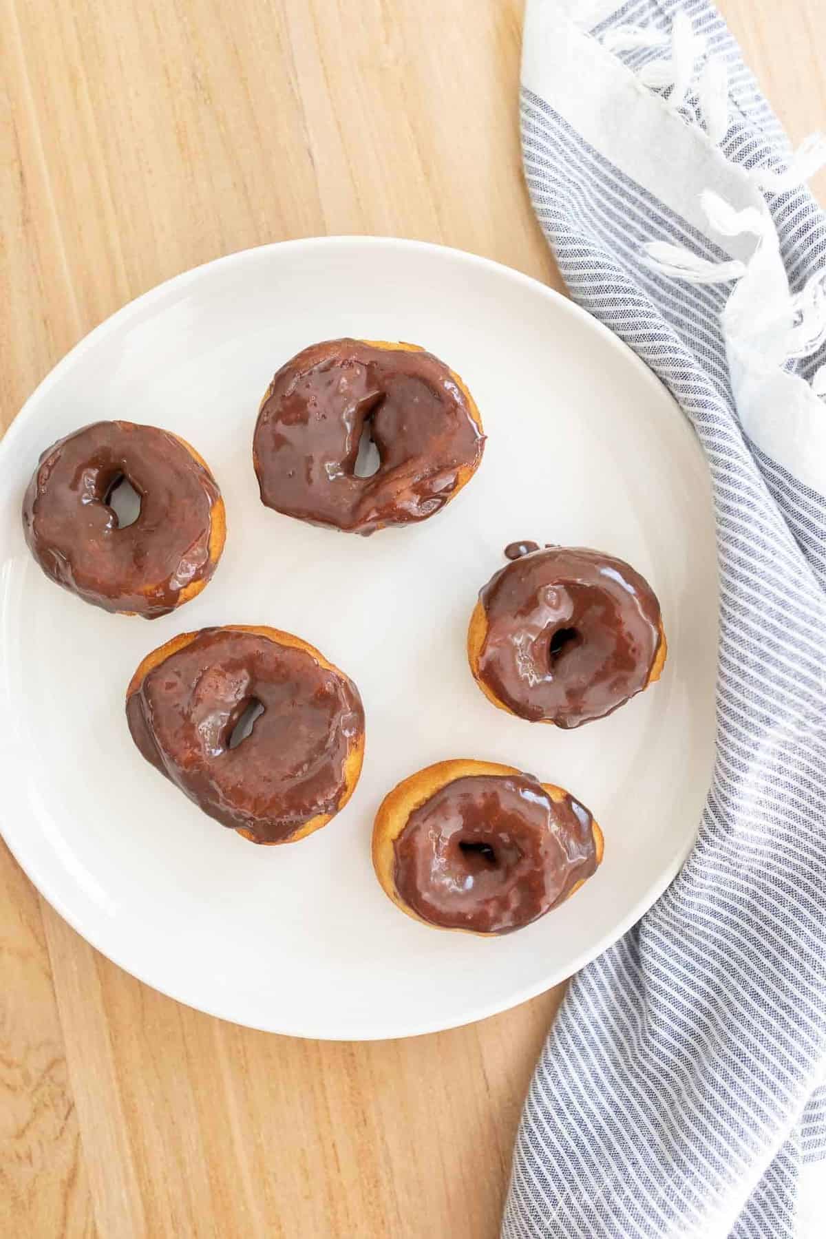 Biscuit donuts covered in chocolate icing on a white plate.