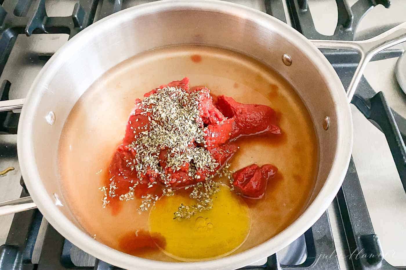 A silver saute pan filled with ingredients for homemade pizza sauce on stove top.