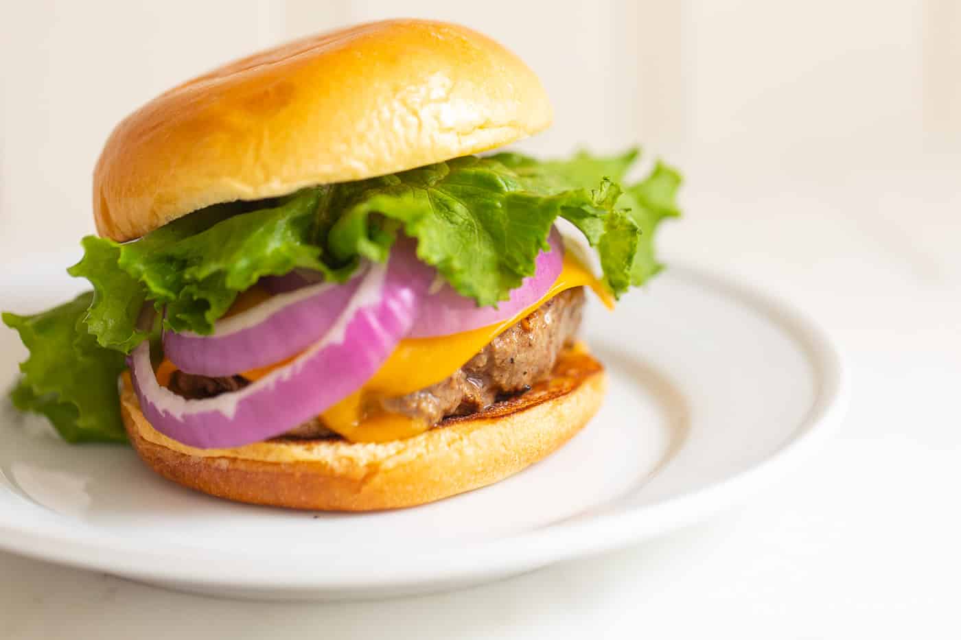 White plate with a cast iron burger stacked with lettuce, red onions and cheese.