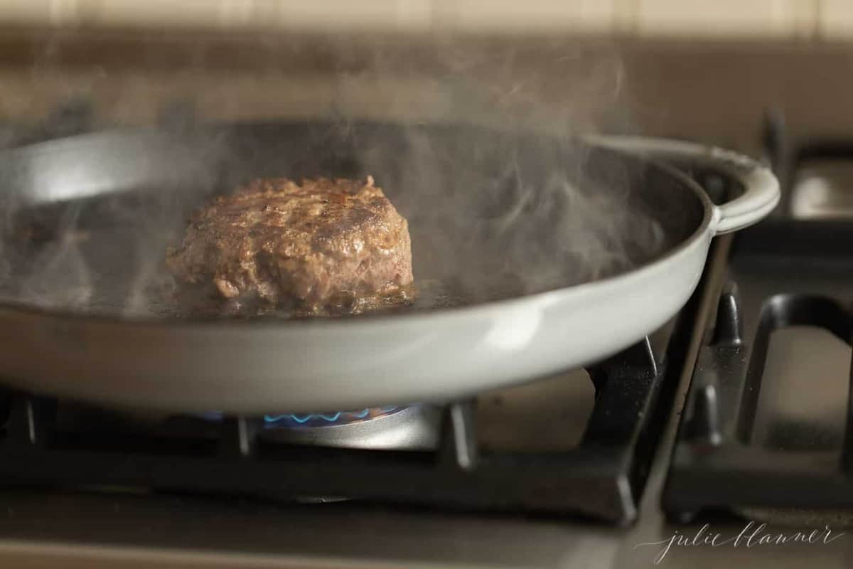 A stovetop burger in a cast iron pan, steam rising.