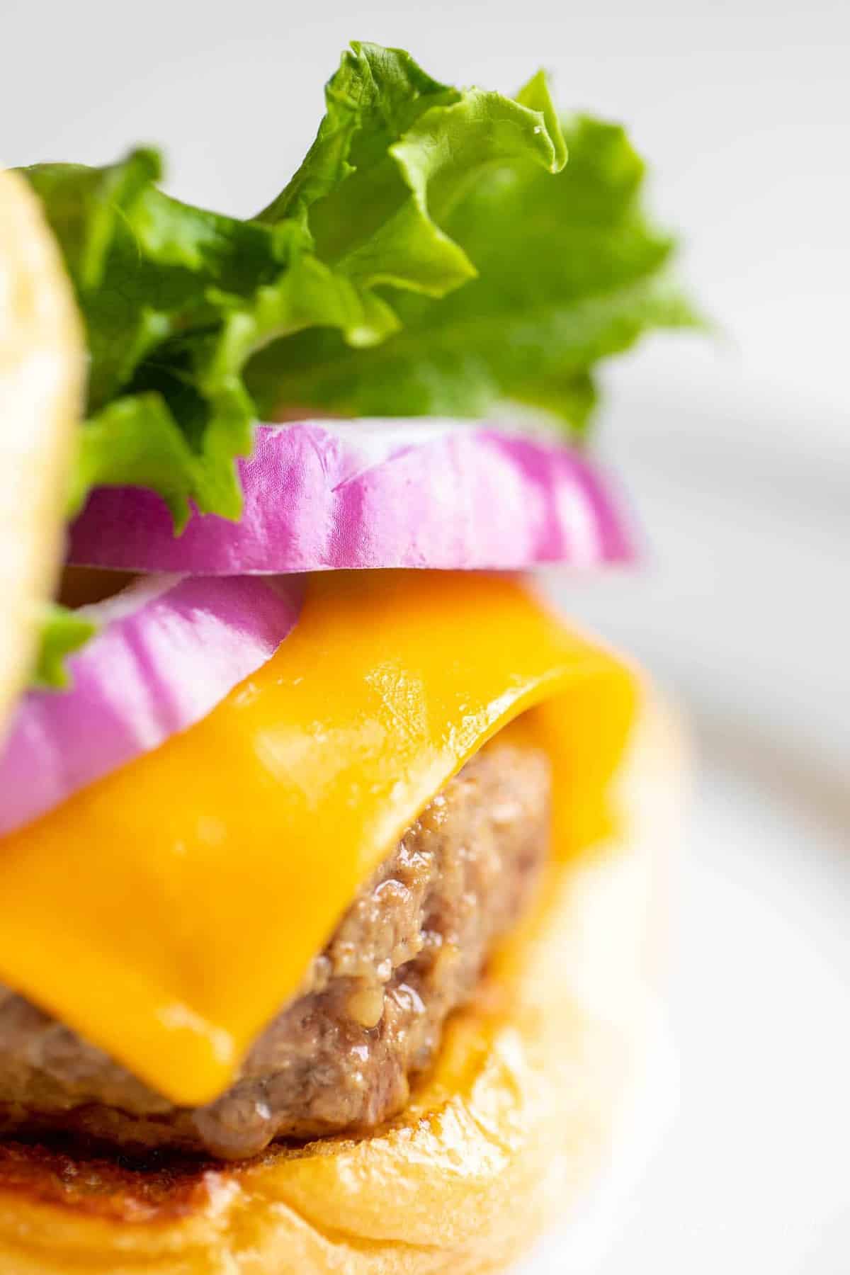 A close up shot of a cast iron burger stacked with lettuce, red onions and cheese.