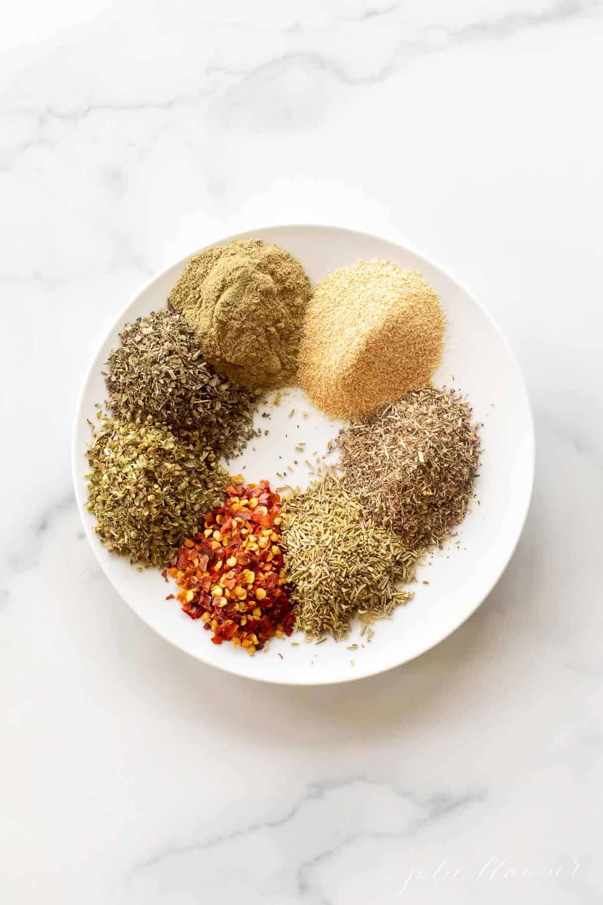 A white plate full of piles of italian herbs and spices.