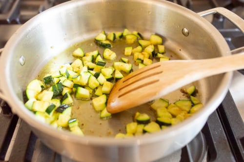 Vegetables cooking in a stainless steel pan on a stovetop.