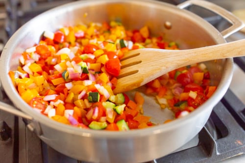 Vegetables cooking in a stainless steel pan on a stovetop.