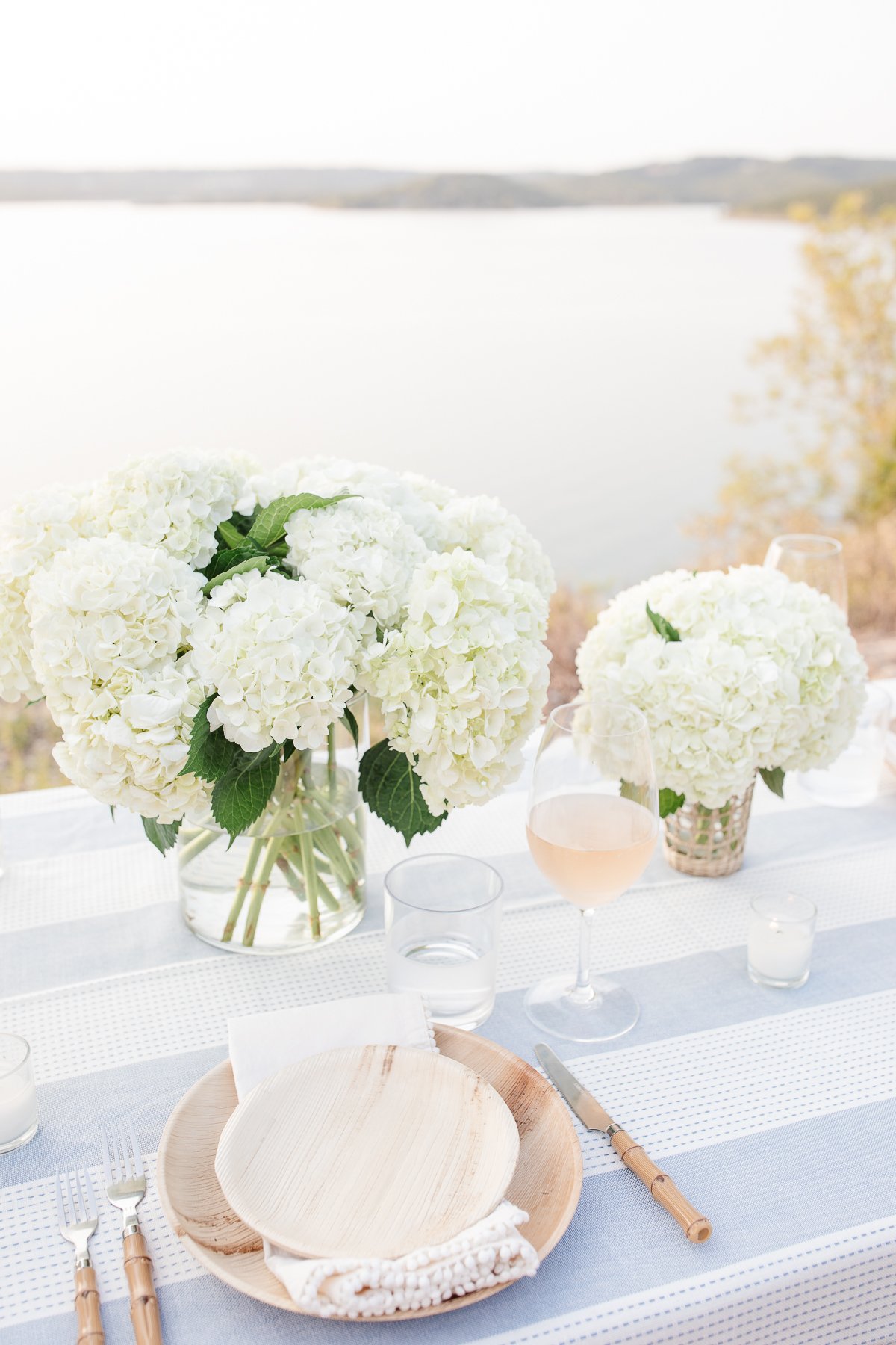 Elegant outdoor dining setup featuring lush hydrangea centerpieces on a table overlooking a serene lake.