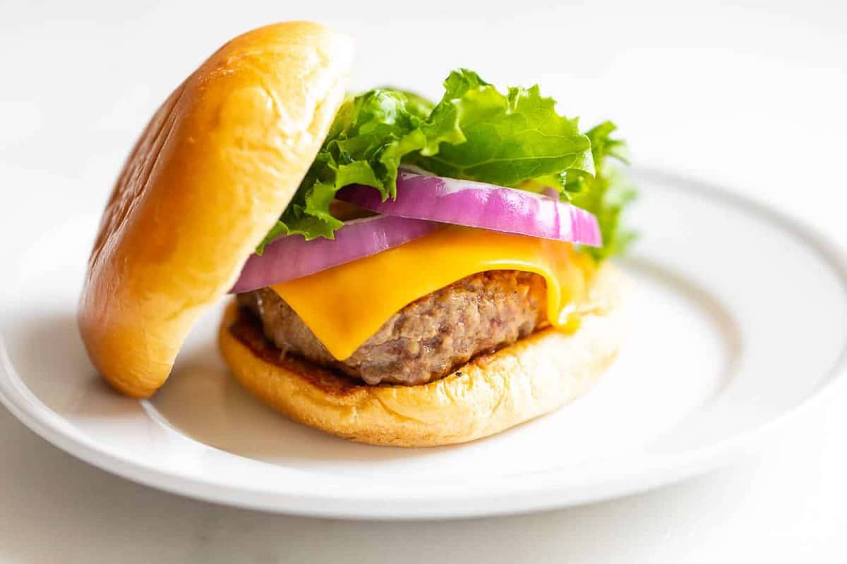 White plate with a cast iron burger stacked with lettuce, red onions and cheese.