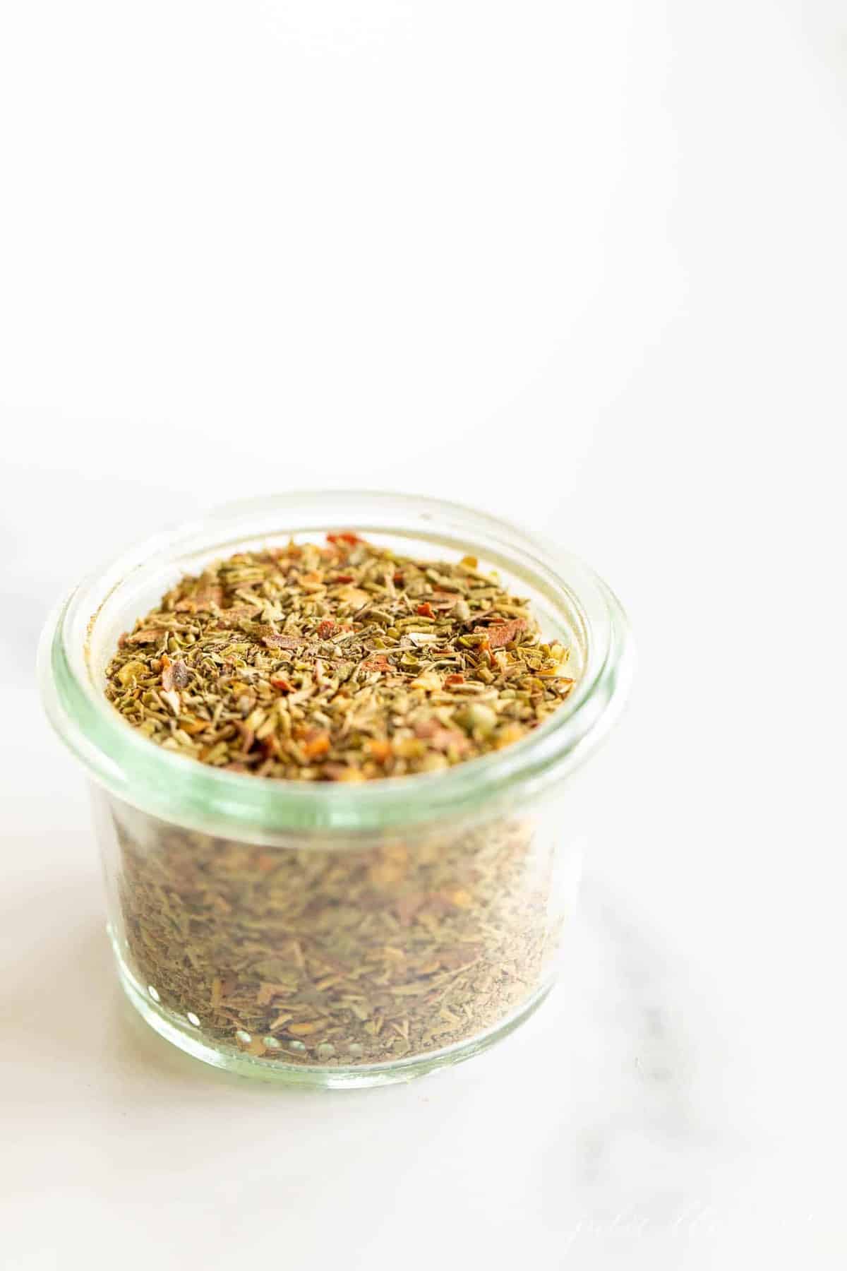 Homemade Italian seasoning in a glass bowl on a marble surface.  