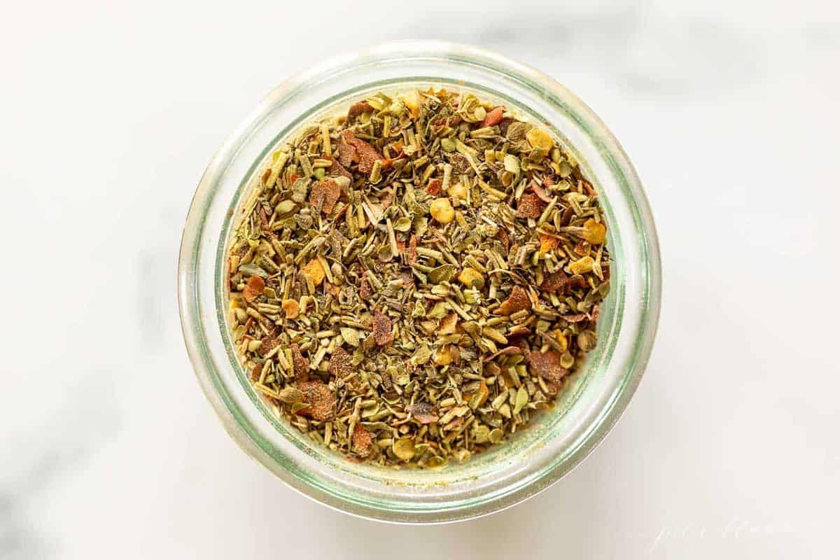 A clear glass jar of italian seasoning blend.