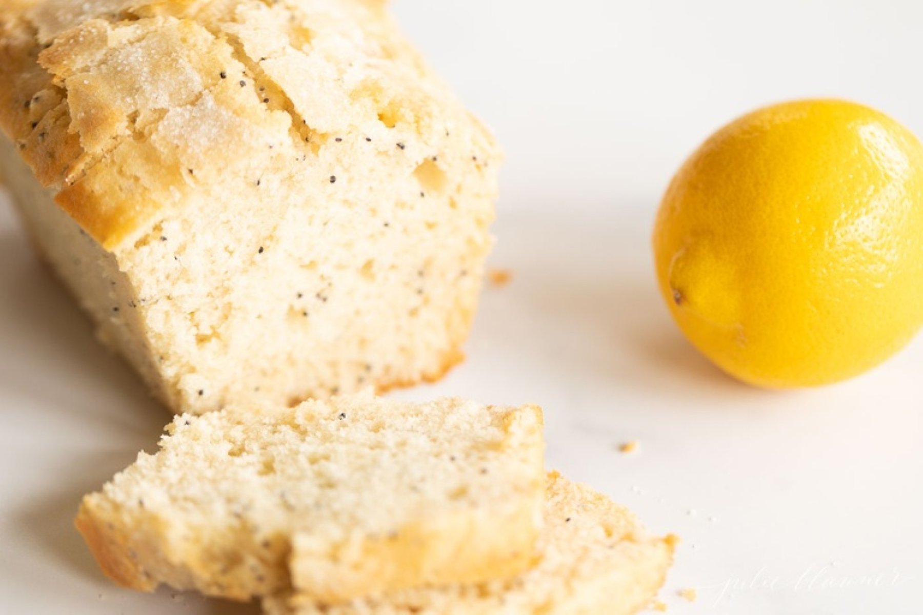 A loaf of lemon poppy seed bread, sliced, with a lemon beside it.