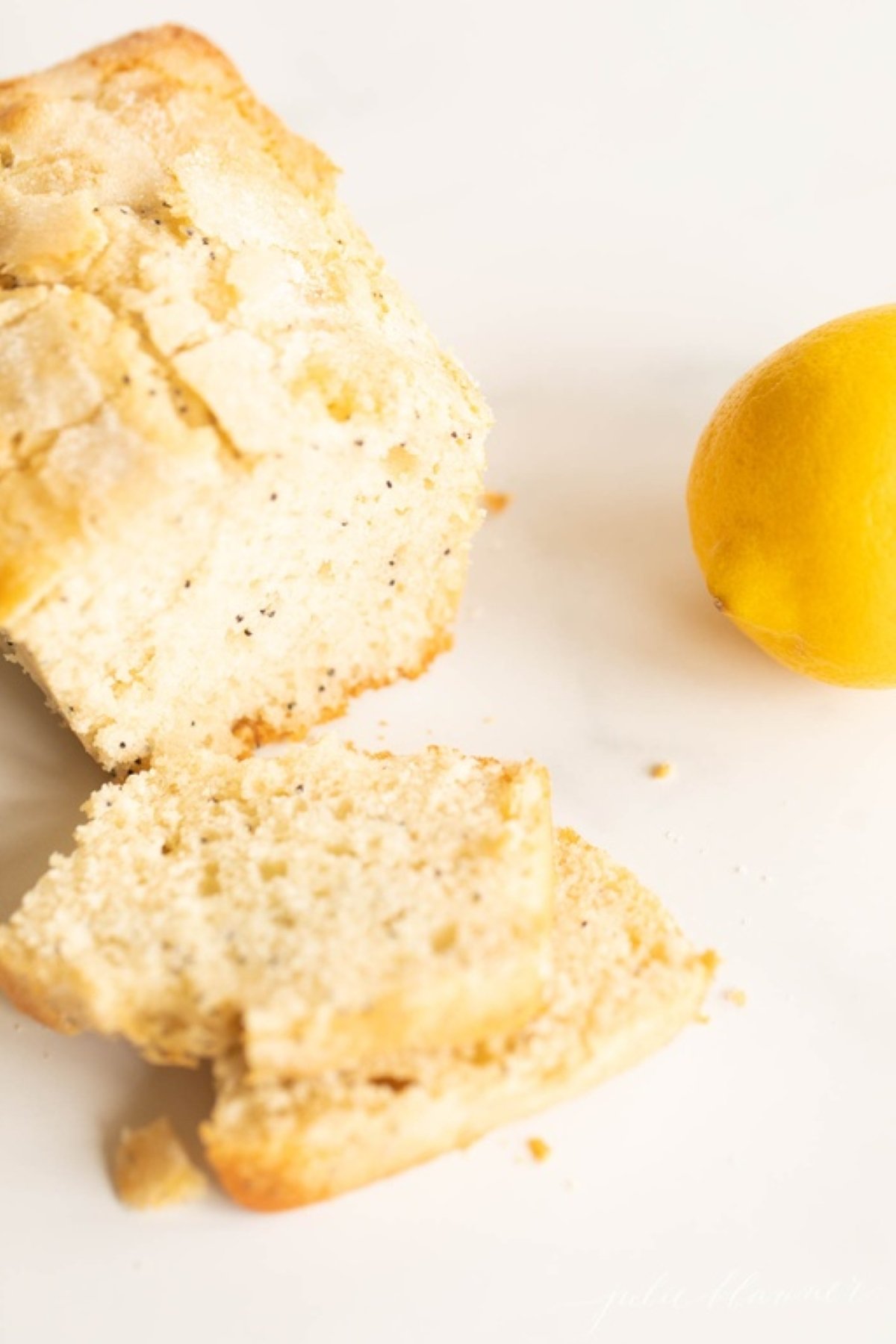 A loaf of lemon poppy seed bread, sliced, with a lemon beside it.