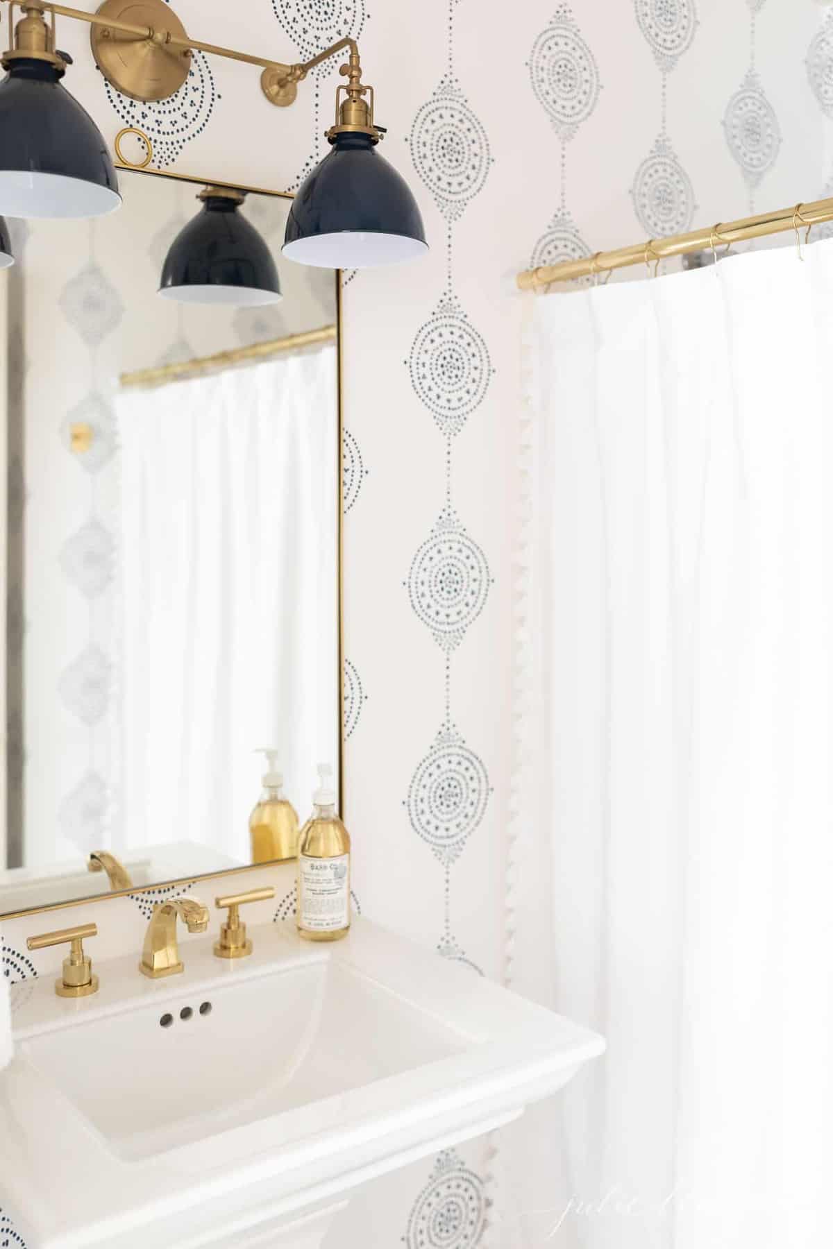 A modern bathroom with a navy light fixture and navy and white patterned bathroom wallpaper.