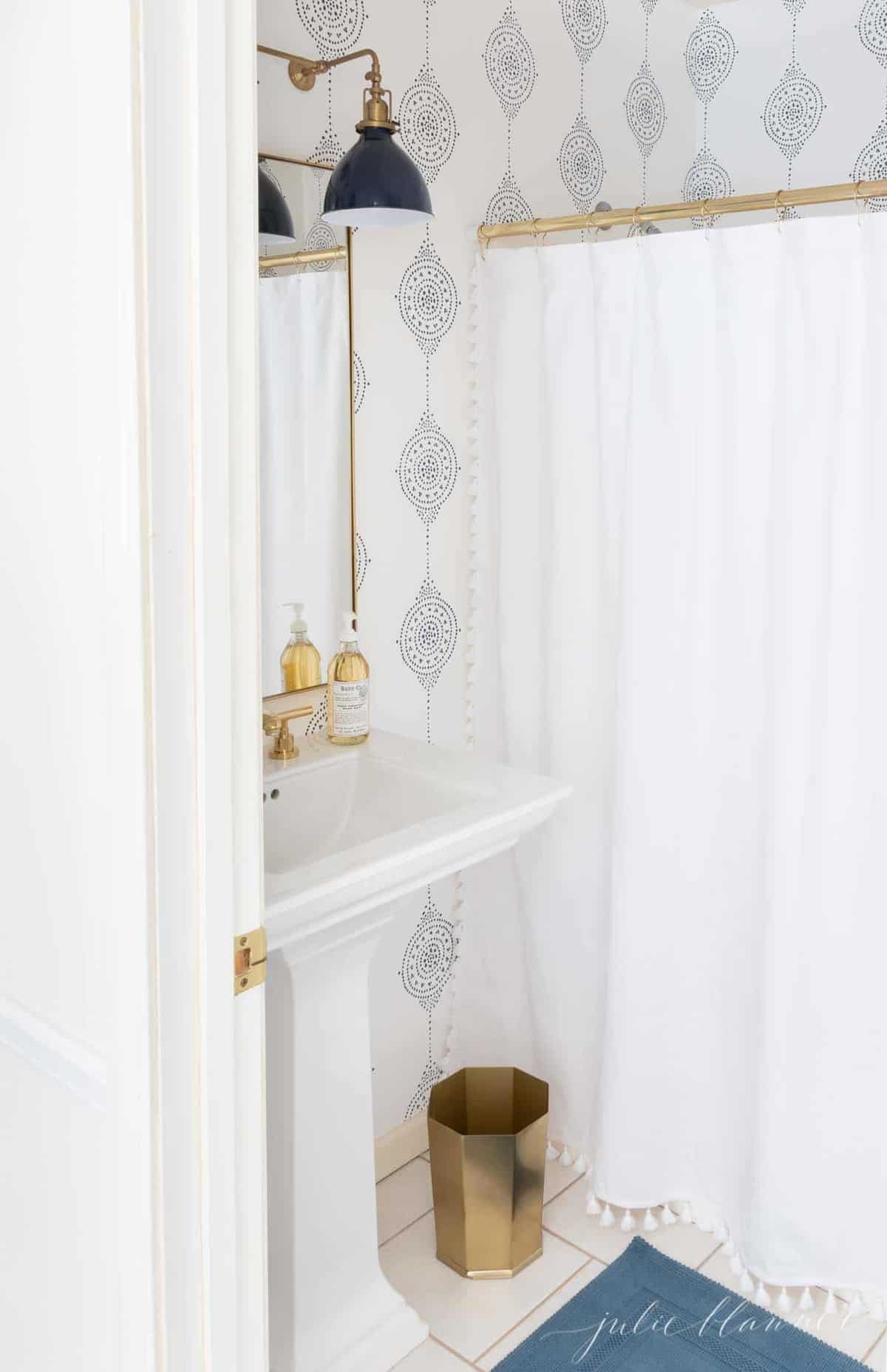 A modern bathroom with a navy light fixture and navy and white patterned bathroom wallpaper.