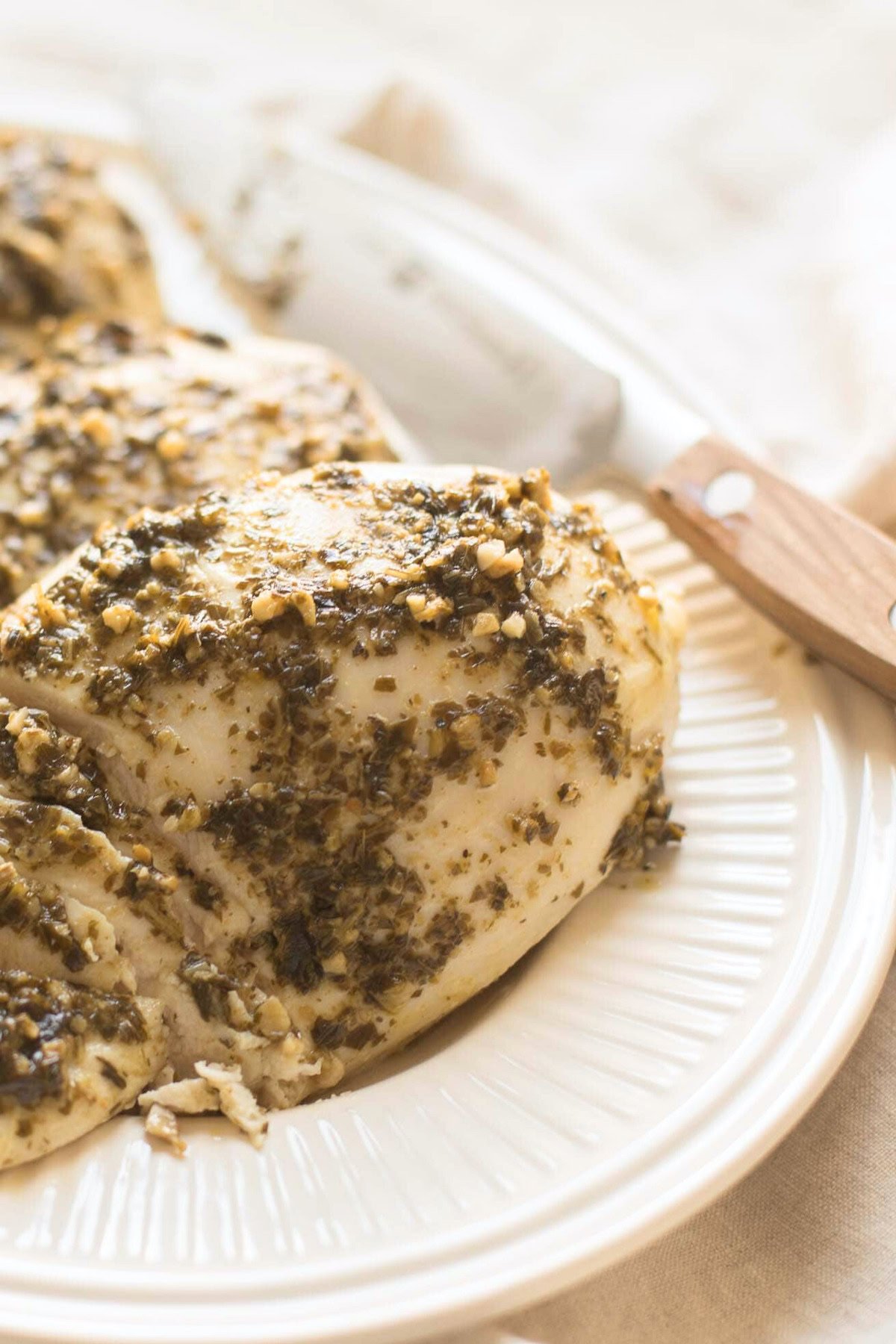 Pesto chicken breasts seasoned with herbs and spices, served on a white ceramic plate with a wooden-handled knife beside it.