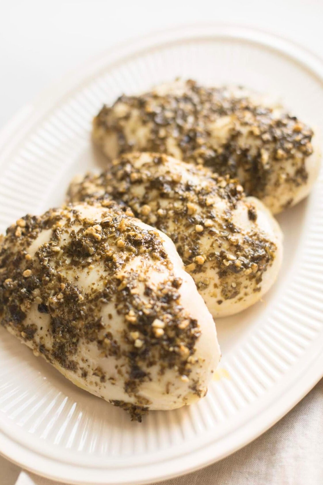 Three seasoned and cooked pesto chicken breasts served on a white plate.