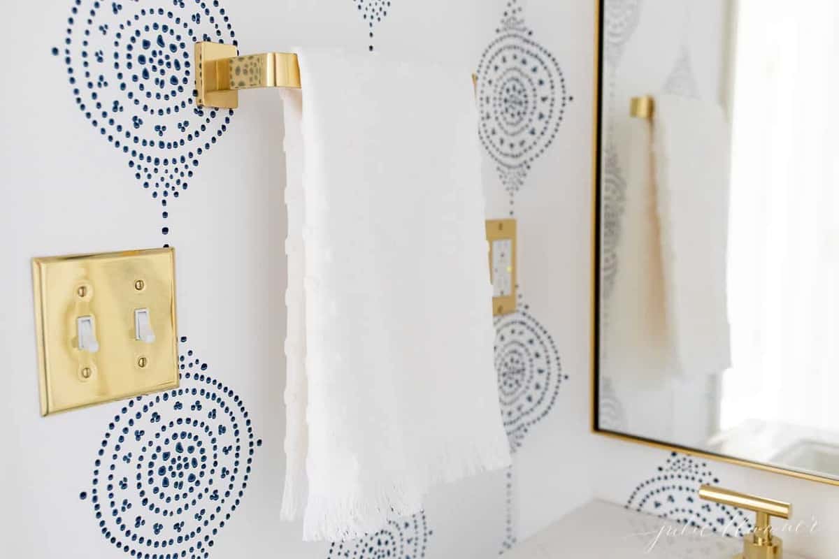 A blue and white walppapered bathroom with a gold towel bar.