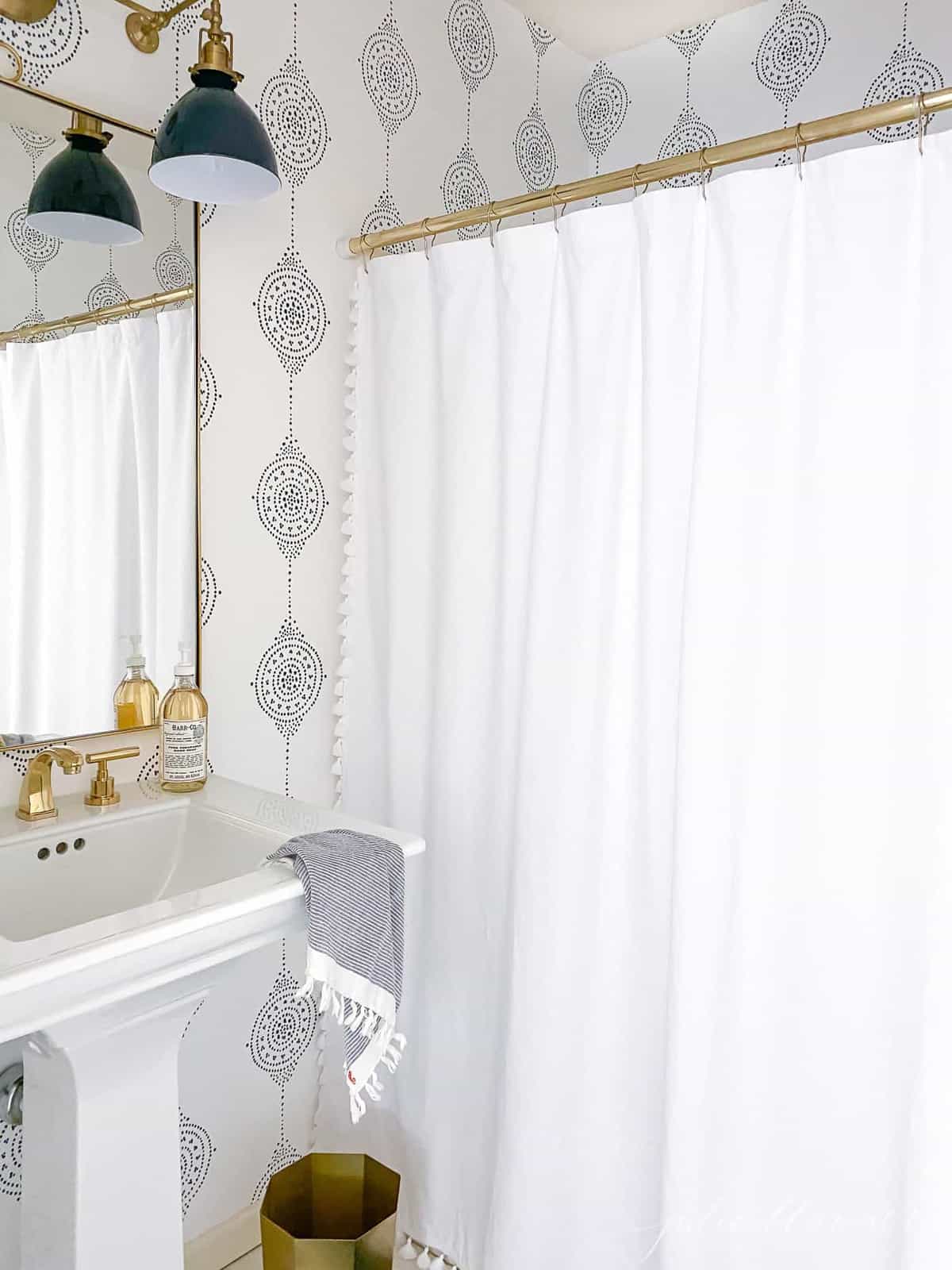 A modern bathroom with a navy light fixture and navy and white patterned bathroom wallpaper.