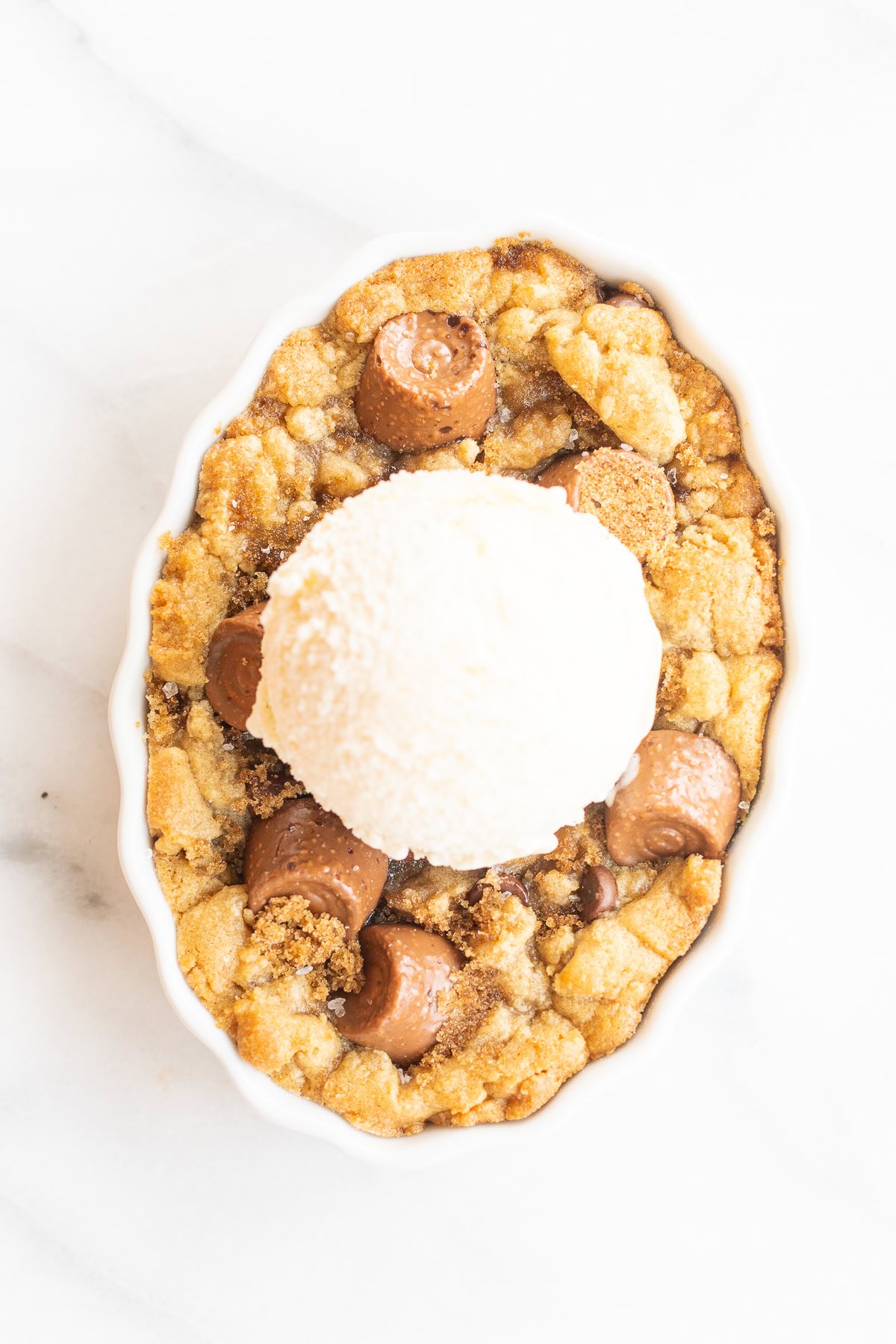 A chocolate chip cobbler topped with a scoop of vanilla ice cream, featuring a crumbly, golden-brown base with pieces of chocolate.