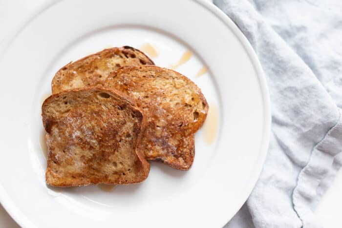 Apple fritter french toast topped with syrup on a white plate.