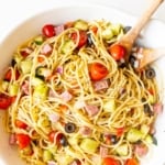 Spaghetti salad in a white bowl with wooden spoons for serving.
