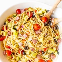 Spaghetti salad in a white bowl with wooden spoons for serving.