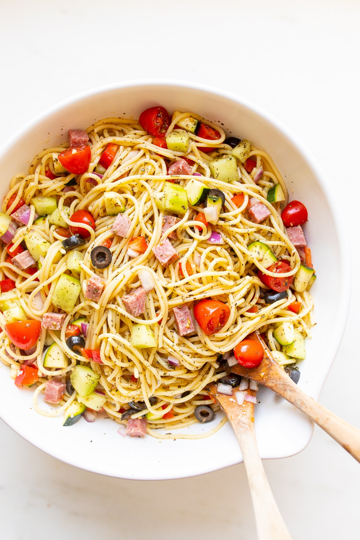 Spaghetti salad in a white bowl with wooden spoons for serving.