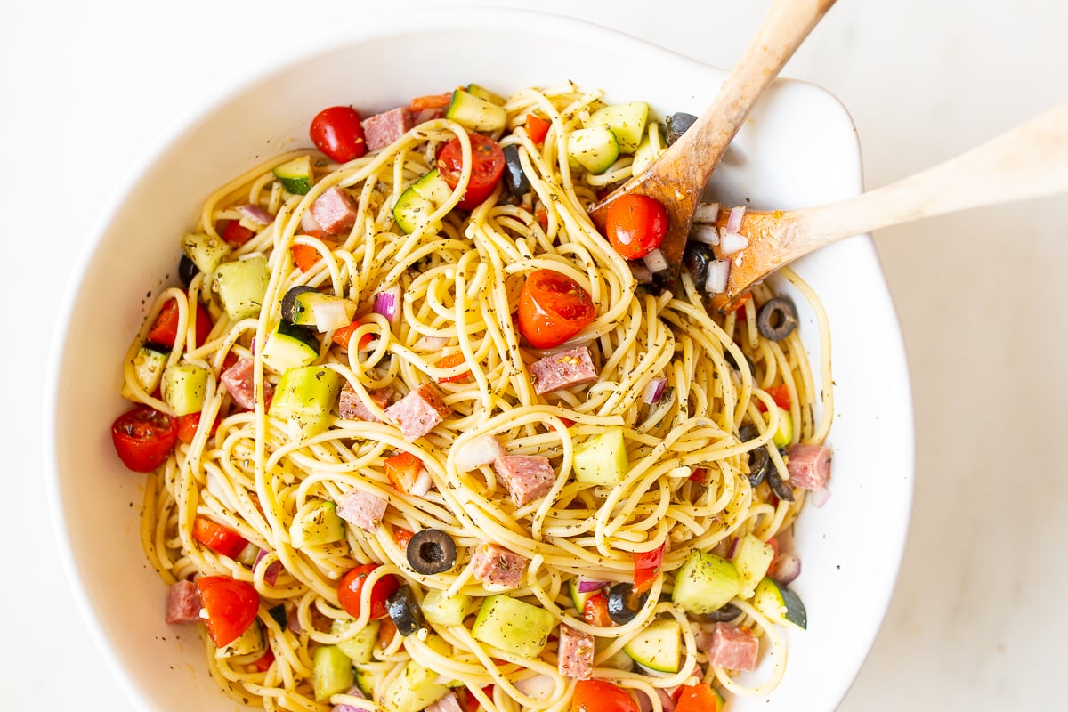 Spaghetti salad in a white bowl with wooden spoons for serving.