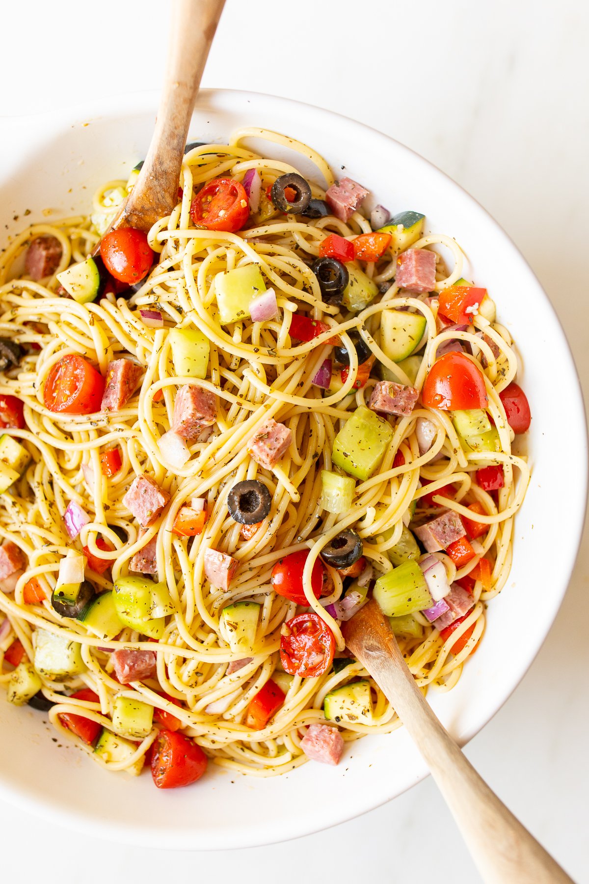Spaghetti salad in a white bowl with wooden spoons for serving.