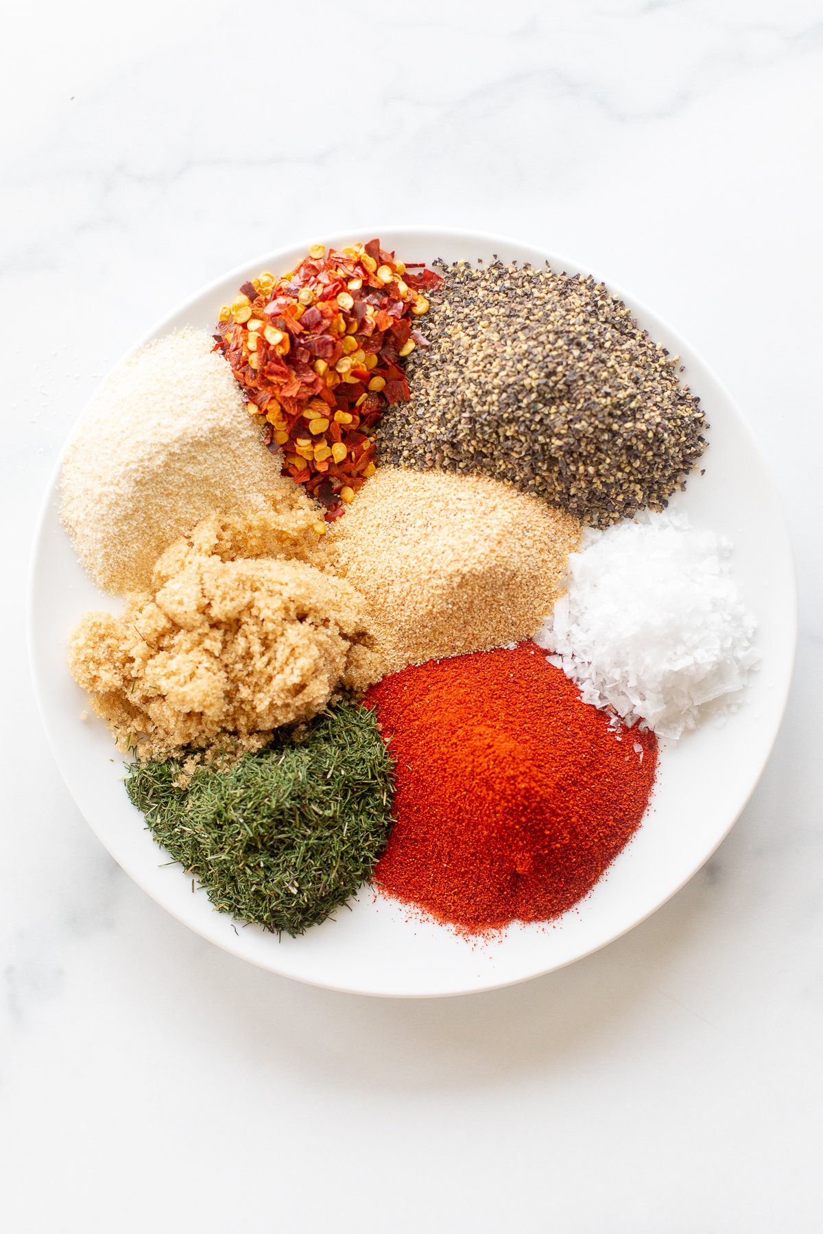 A white plate with various spices and Steak Seasoning on it.