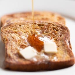 Close up shot of apple fritter french bread, pats of butter on top and syrup being poured.