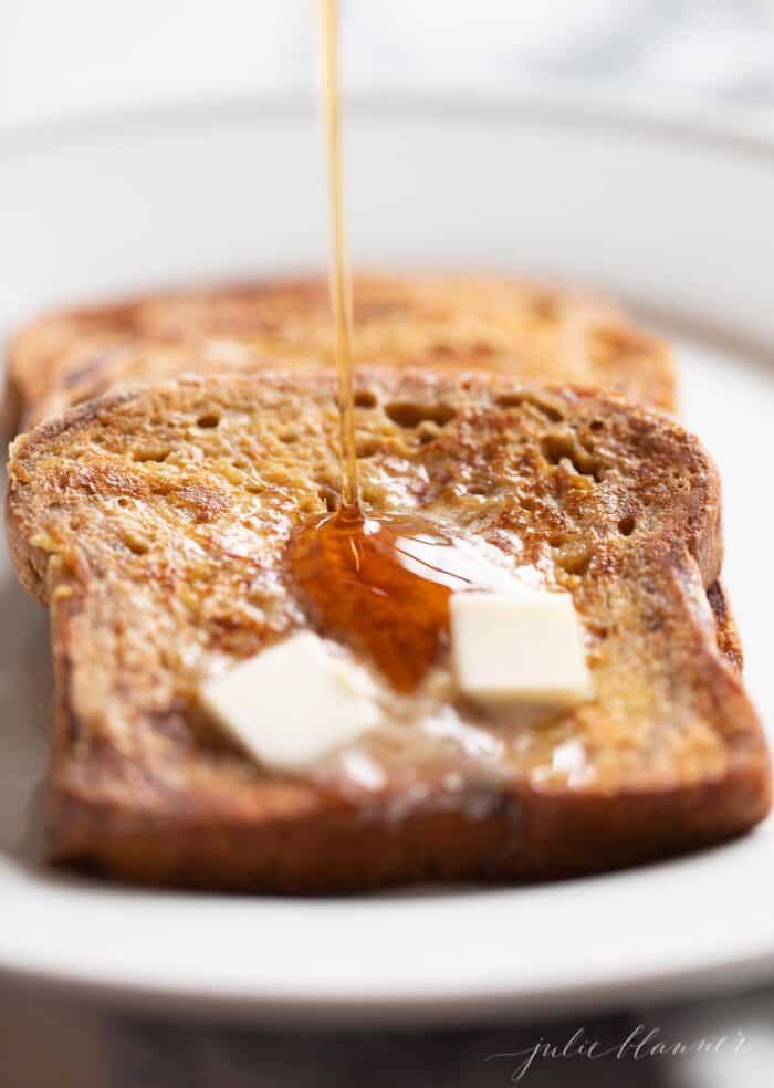 Apple fritter french toast topped with butter and syrup on a white plate.